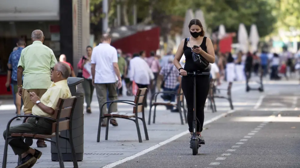 Una chica mira el móvil mientras circula en patinete este jueves en Zaragoza.