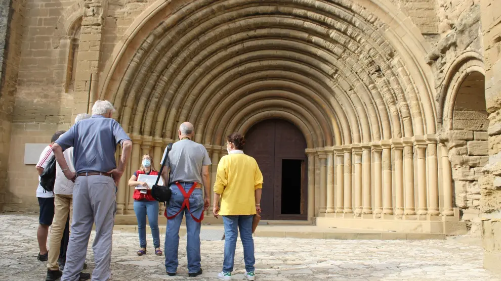 Los visitantes atienden las explicaciones de la guía frente a la portada de la iglesia del monasterio.