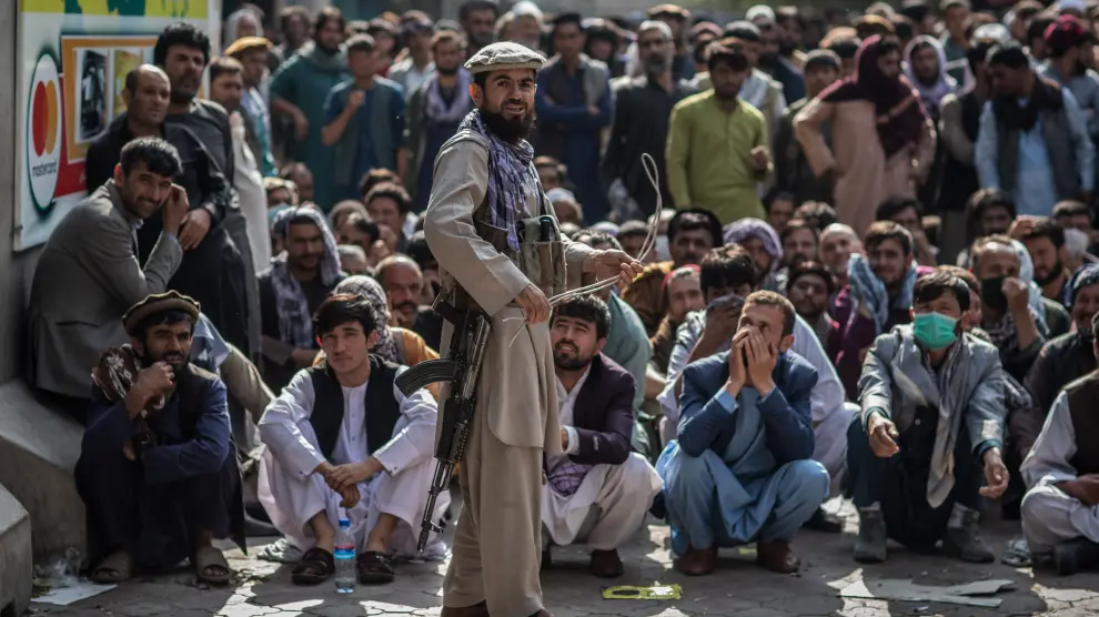 Un talibán, delante de un grupo de hombres que esperan que abra un banco para sacar dinero, en Kabul