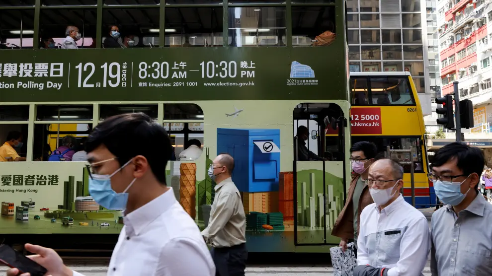 People walk in front of a tram with an advertisement about upcoming Legislative Council election in Hong Kong
