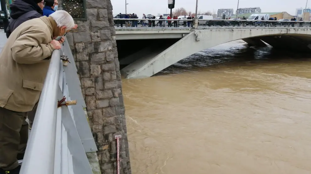 Un vecino de Zaragoza se asoma para ver la altura del caudal que alcanza el Ebro a su paso por el puente de Santiago.