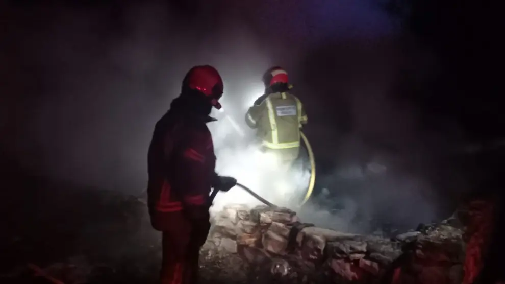 Dos bomberos, trabajando en la extinción del incendio, que se declaró por la noche.