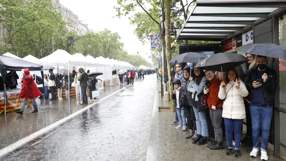 Ciudadanos se resguardan del chaparrón tras desafíar a la lluvia y visitar las casetas de venta de libros en el Paseo de Gràcia