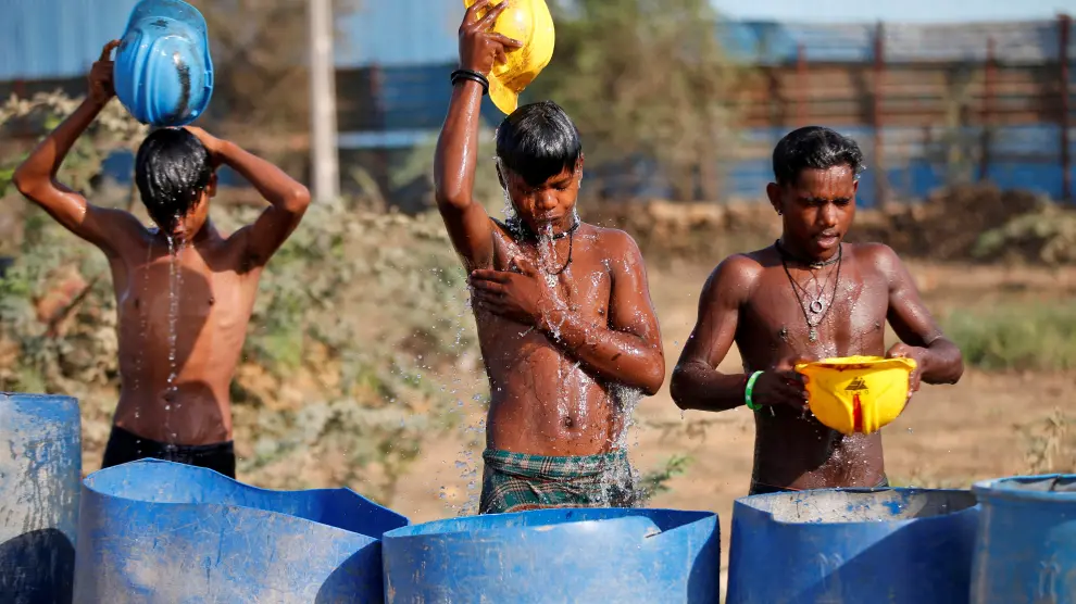 Workers use their helmets to pour water to cool off near a construction site on a hot summer day on the outskirts of Ahmedabad