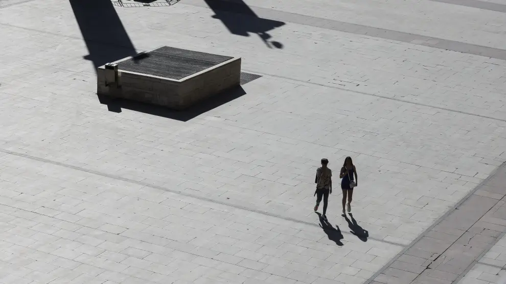 Dos personas caminan por una plaza del Pilar desierta por el calor