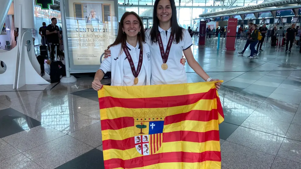 Irene Samper y María Sanz posan con la bandera de Aragón y las medallas de campeonas de Europa en el aeropuerto de Oporto.