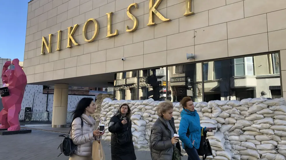 Varias mujeres pasan por delante del centro comercial Nikolsky protegido por sacos terreros.