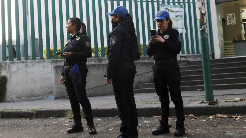 Police officers hold their smartphones as they stand along the street after a tremor was felt in Mexico City