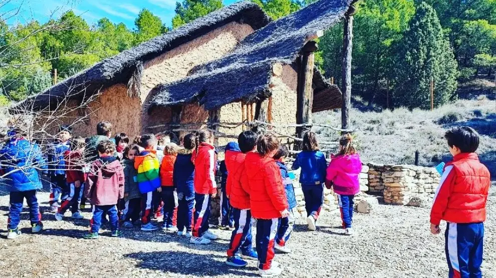 Un grupo de escolares junto a la recreación de la cabaña de la Edad de Hierro del parque.