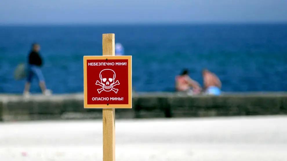 Imagen de una playa de Ucrania con un cartel que avisa del peligro de bombas.