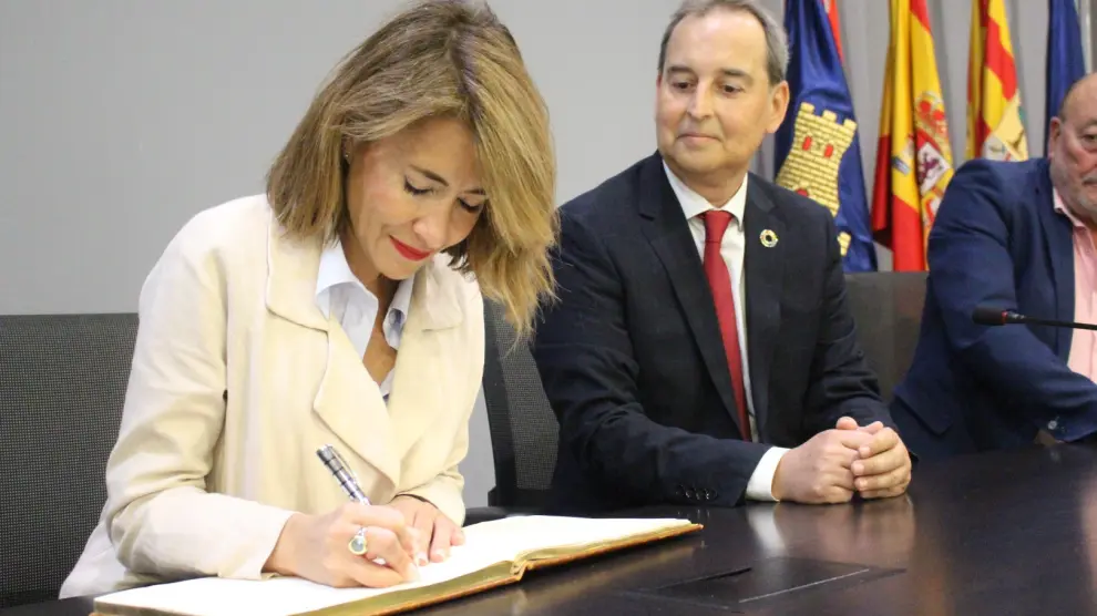 La ministra Raquel Sánchez firma en el Libro de Honor del Ayuntamiento de Binéfar bajo la mirada del alcalde, Alfonso Adán.