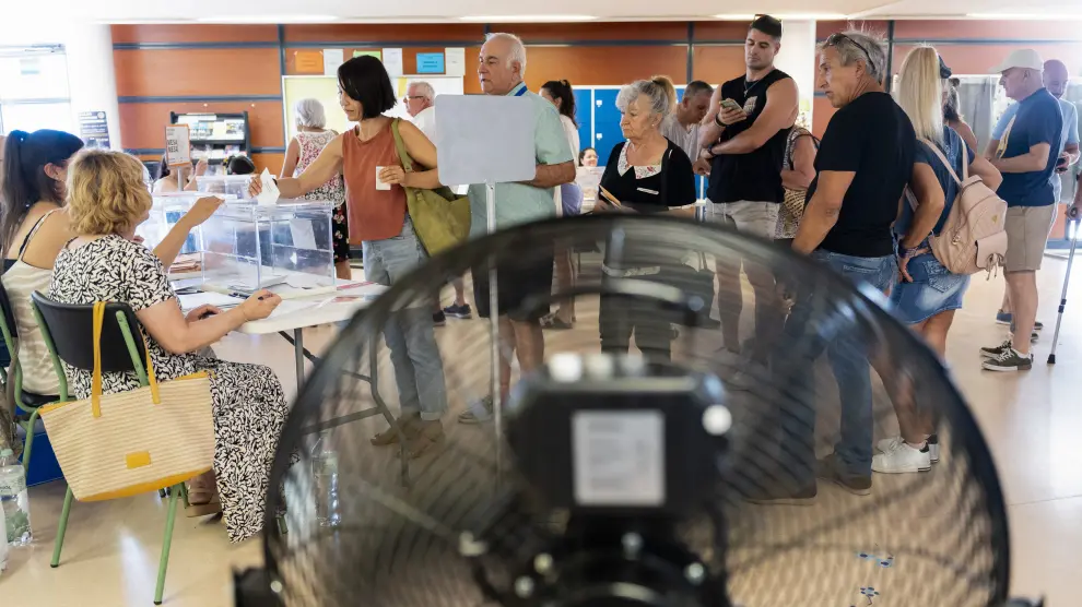 Votantes hacen cola ante su mesa situada cerca de un ventilador para combatir el calor en un colegio electoral en Pineda de Mar.