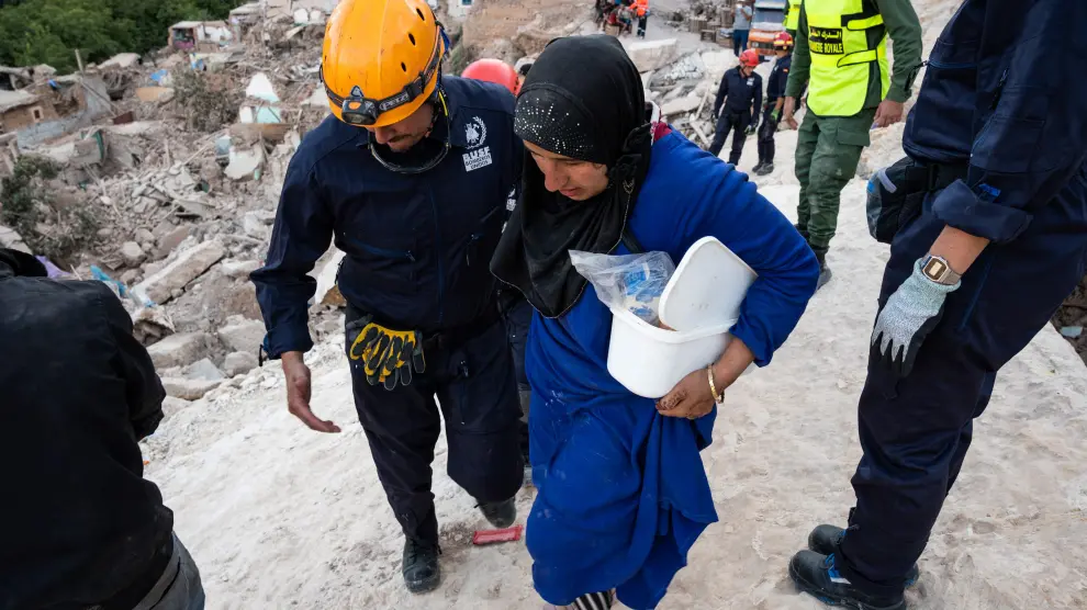 Un bombero de la ONG Busf ayuda a una mujer a caminar por una zona destruida del terremoto.