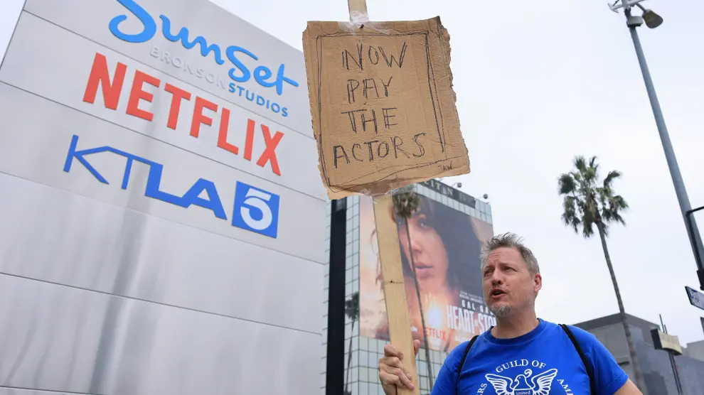 El guionista estadounidense Travis Adam Wright, apoyando al Screen Actors Guild, camina con un cartel casero delante de Netflix en Hollywood.