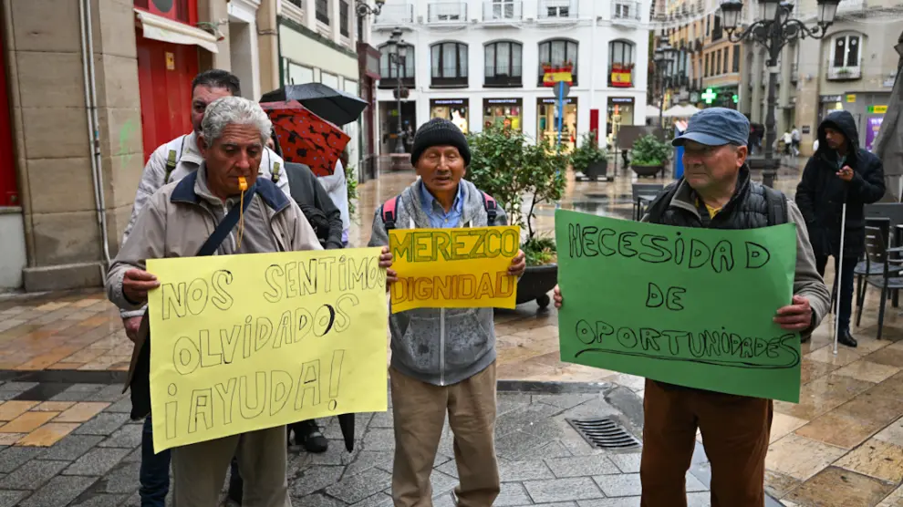 Tres de los participantes en la marcha de las personas sin hogar muestran sus pancartas reivindicativas