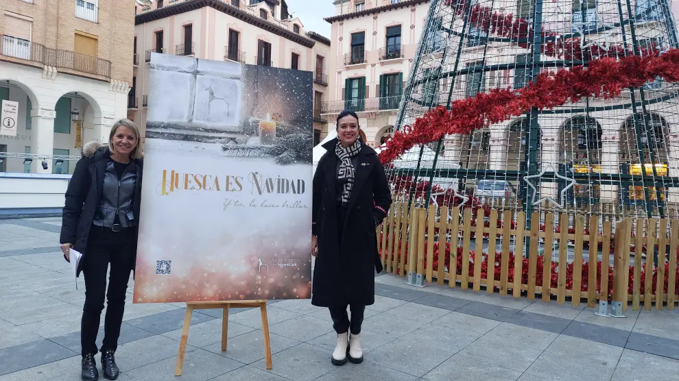La concejala Nuria Mur y la alcaldesa de Huesca, Lorena Orduna, junto al cartel de Navidad en la plaza López Allué.
