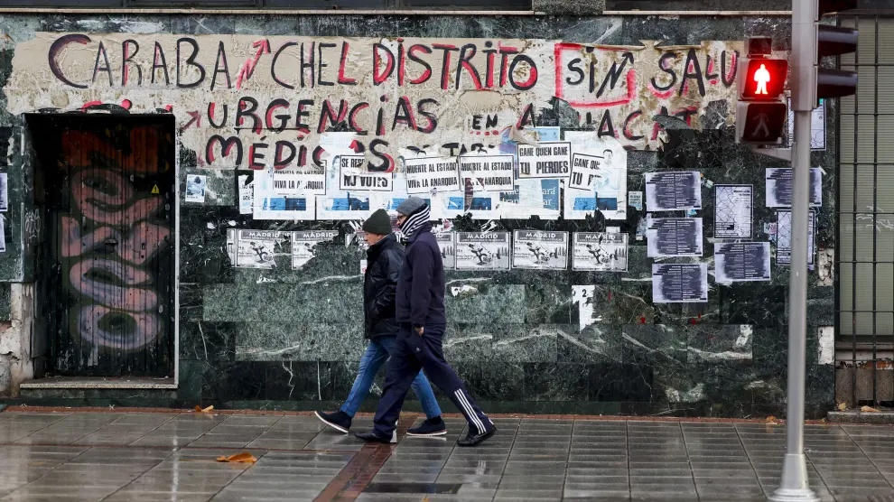 Dos personas pasan ante una pintada que reivindica la Sanidad pública en Madrid, en plena saturación de los centros de salud por la epidemia estacional de virus respiratorios, como la gripe o la covid.