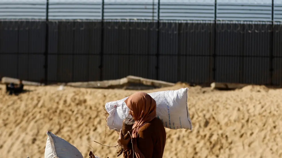 A woman carries a sack and wood as displaced Palestinians, who fled their houses due to Israeli strikes, shelter at a tent camp in Rafah, amid the ongoing conflict between Israel and the Palestinian Islamist group Hamas, in the southern Gaza Strip, January 10, 2024. REUTERS/Ibraheem Abu Mustafa [[[REUTERS VOCENTO]]]