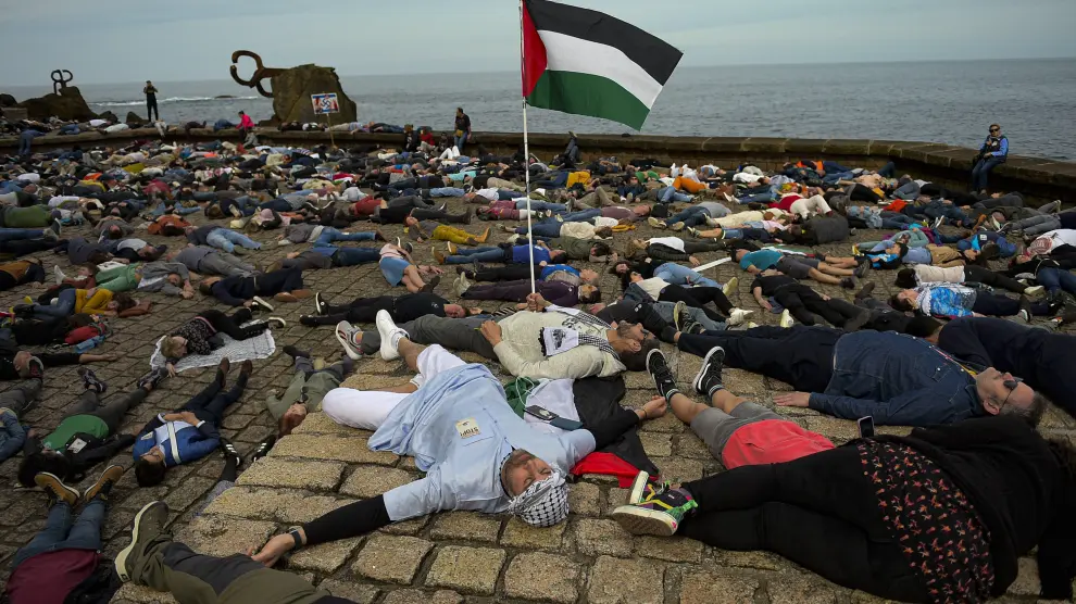 Miles de personas tumbadas junto al Peine de los Vientos en protesta por la guerra en Gaza