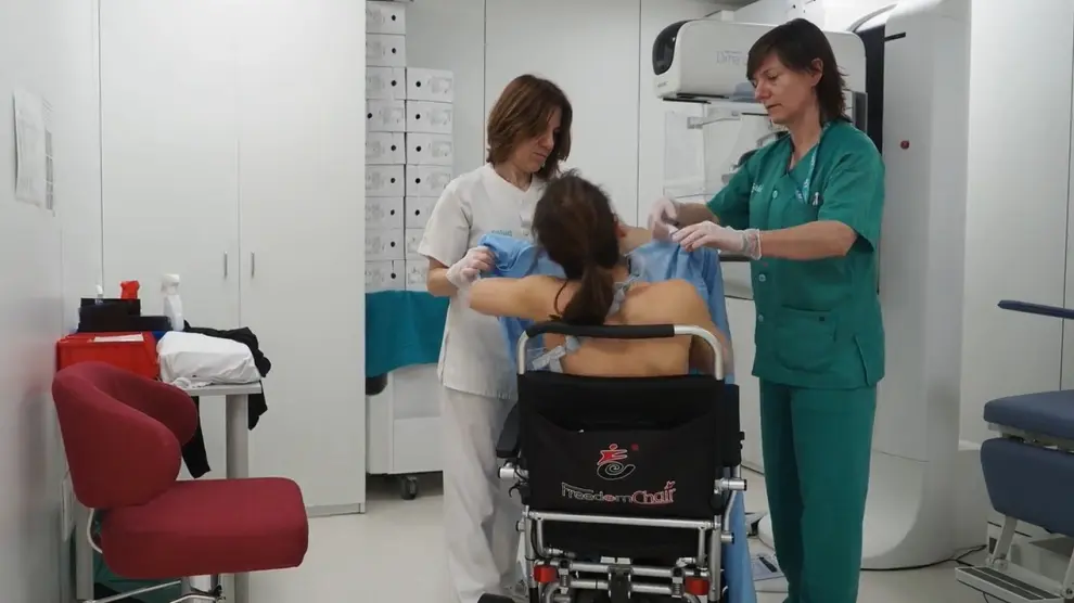 Dos profesionales ayudan a una paciente con discapacidad a cambiar de silla para realizar una mamografía en el Hospital Miguel Servet.