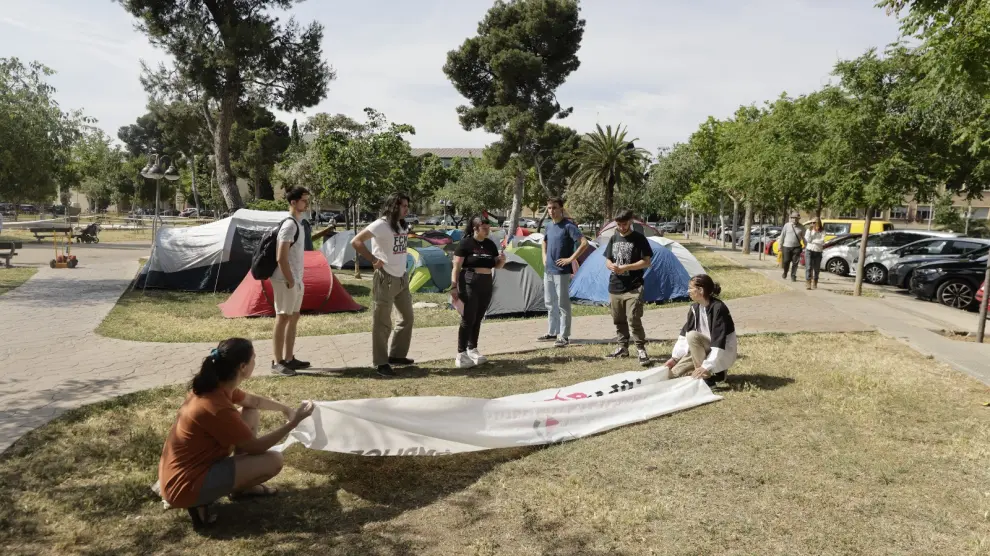 Un grupo de estudiantes prepara una pancarta junto al campamento instalado en la zona del estanque del campus de Zaragoza