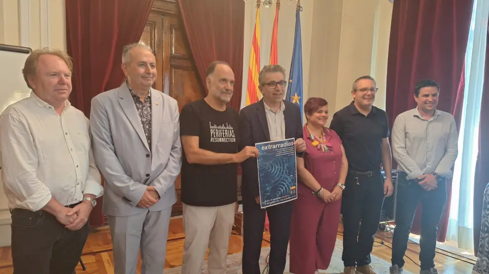 Jordi Martí, con Luis Lles a su derecha, muestra el cartel de Extrarradios, en la subdelegación del Gobierno en Huesca
