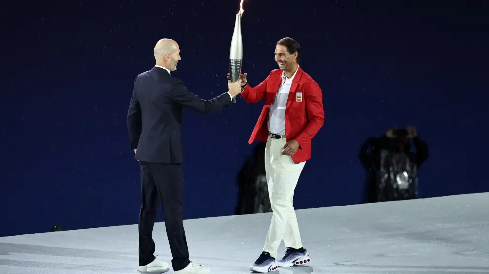 Paris (France), 26/07/2024.- French former soccer player Zinedine Zidane (L) hands over the Olympic Torch to tennis player Rafael Nadal of Spain during the Opening Ceremony of the Paris 2024 Olympic Games, in Paris, France, 26 July 2024. (Tenis, Francia, España) EFE/EPA/CHRISTOPHE PETIT TESSON