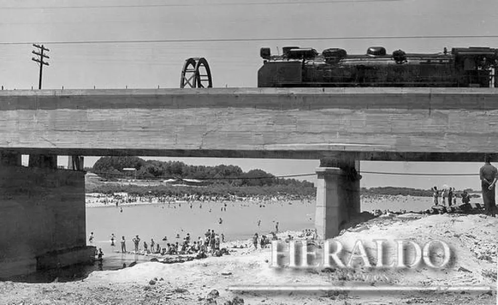 Obras de construcción del nuevo paso de trenes en el puente de la Almozara en 1949. En la parte inferior, bañistas en la playa del Ángel del río Ebro