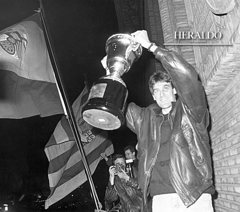 El CAI fue recibido el 14 de febrero de 1990 en la plaza del Pilar de Zaragoza con honores tras vencer al Joventut (76-69) y conseguir por segunda vez en su historia el título de campeón de la Copa del Rey. Alrededor de 5.000 personas se dieron cita para aplaudir y homenajear al club. En la fotografía, el capitán del equipo, Fernando Arcega, levantando la copa desde el balcón del Ayuntamiento ante la multitud que coreaba el nombre del equipo.