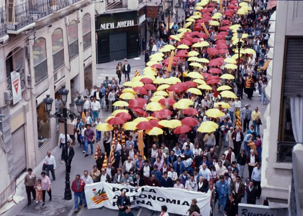 Manifestantes cubiertos por sus paraguas rojos y amarillos por la calle Alfonso de Zaragoza