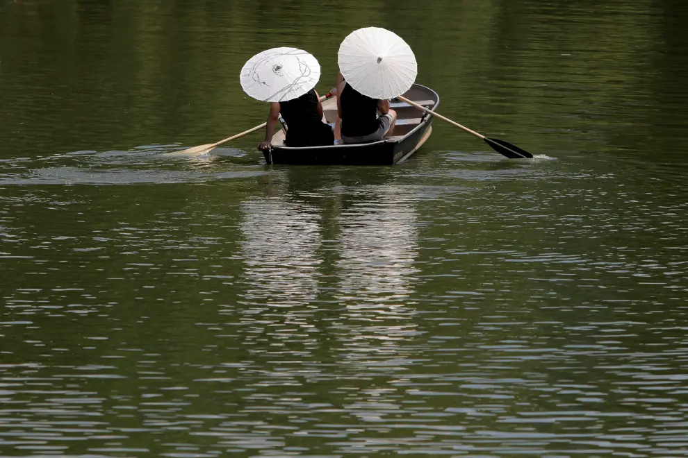 Dos personas se protegen con sus parasoles mientras pasean en barca por Central Park.