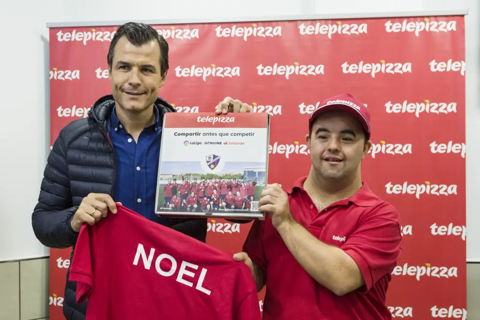 El histórico jugador de la SD Huesca y miembro de la Fundación Alcoraz, Juanjo Camacho, le hizo entrega a Noel Esteban de la caja solidaria que Telepizza creó con motivo del acto.