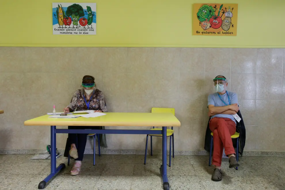 Officials, wearing protective face masks, wait for voters at a polling station during Galicia's regional elections in Ribadeo
