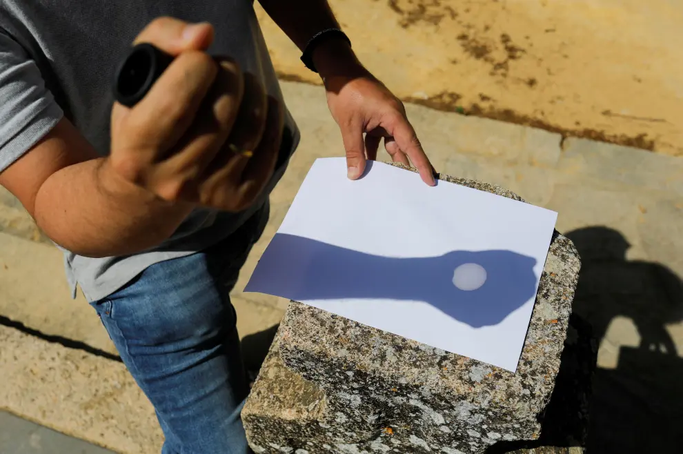 A man uses a monocular to cast a reflection of a partial solar eclipse on a paper in Ronda