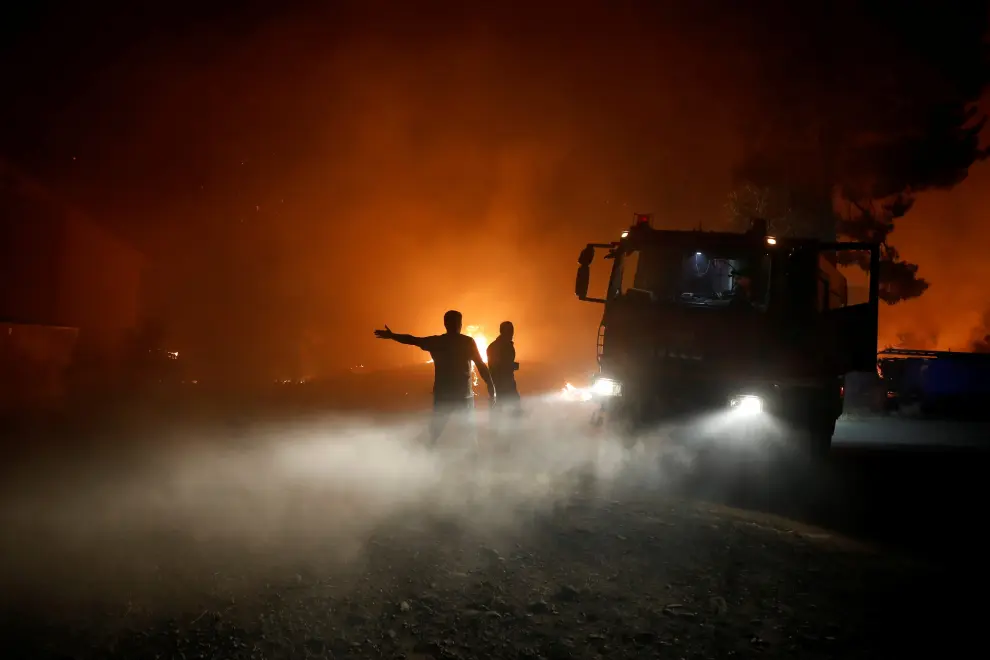 Flames rise next to firefighting vehicles as a wildfire burns in the village of Rovies, on the island of Evia, Greece, August 4, 2021. REUTERS/Costas Baltas[[[REUTERS VOCENTO]]] EUROPE-WEATHER/GREECE-WILDFIRES
