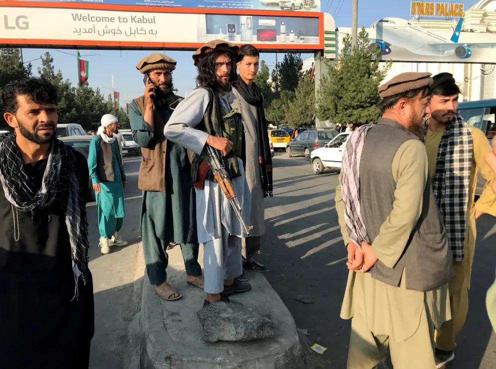 A member of Taliban stands guard as people walk at the entrance gate of Hamid Karzai International Airport in Kabul, Afghanistan, August 16, 2021.REUTERS/Stringer[[[REUTERS VOCENTO]]] AFGHANISTAN-CONFLICT/
