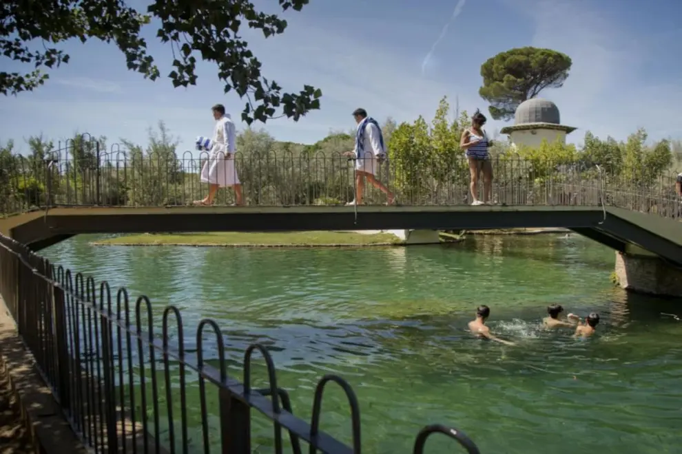 Unos bañistas pasan sobre el puente del lago de un balneario de Alhama de Aragón