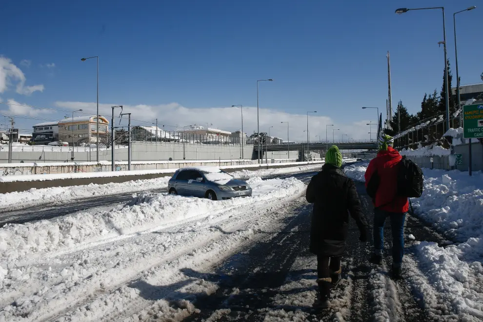 Athens (Greece), 25/01/2022.- A couple walk behind an immobilised car, covered in snow at Attiki odos, the Greek capital's biggest ring road, following a heavy snowfall in Athens, Greece, 25 January 2022. Thousands of motorists are trapped on the highway of Attiki odos in their cars and trucks during the blizzard. A bad weather front, named Elpis by the National Meteorological Services (EMY), has caused frozen temperatures, stormy winds and heavy snowfall since 22 January. (Grecia, Estados Unidos, Atenas) EFE/EPA/YIANNIS KOLESIDIS
 GREECE WEATHER AFTERMATH
