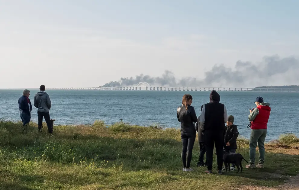 People watch fuel tanks ablaze and damaged sections of the Kerch bridge in the Kerch Strait, Crimea