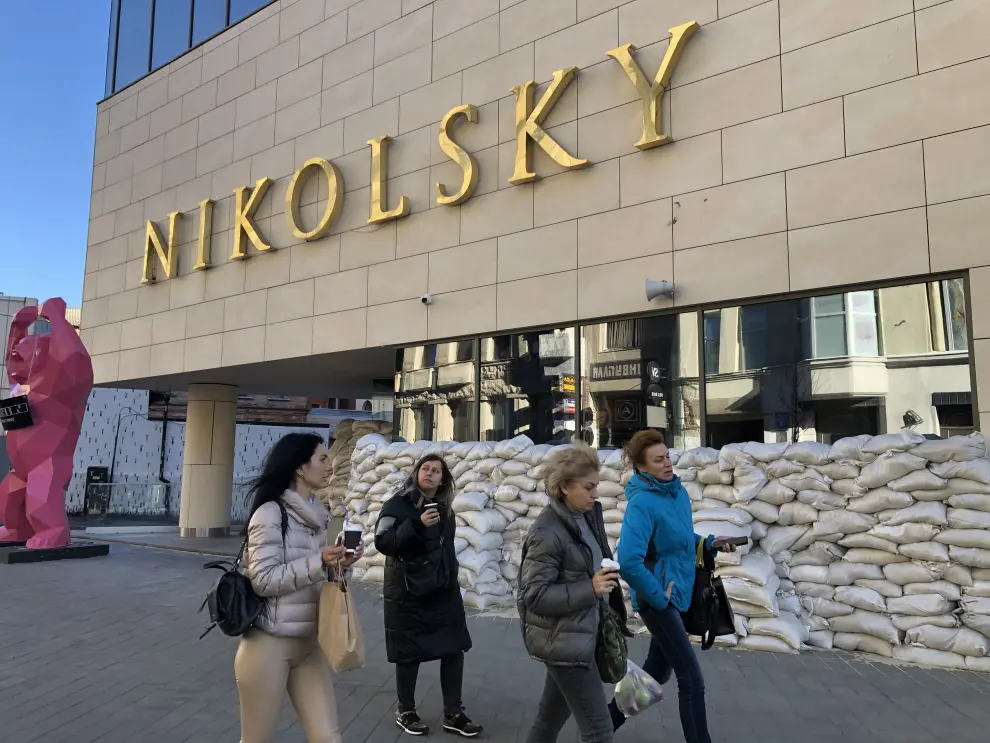 Varias mujeres pasan por delante del centro comercial Nikolsky protegido por sacos terreros.