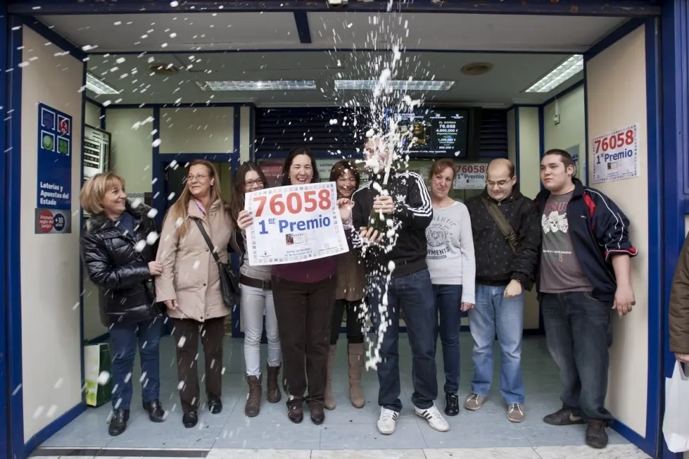 Un Gordo muy repartido pellizcó en 2012 a Zaragoza y Huesca. La titular de la administración 42 del barrio de Las Delicias, con el cartel del premio, y su hijo, con la botella de cava, junto a varios vecinos, celebran el premio.