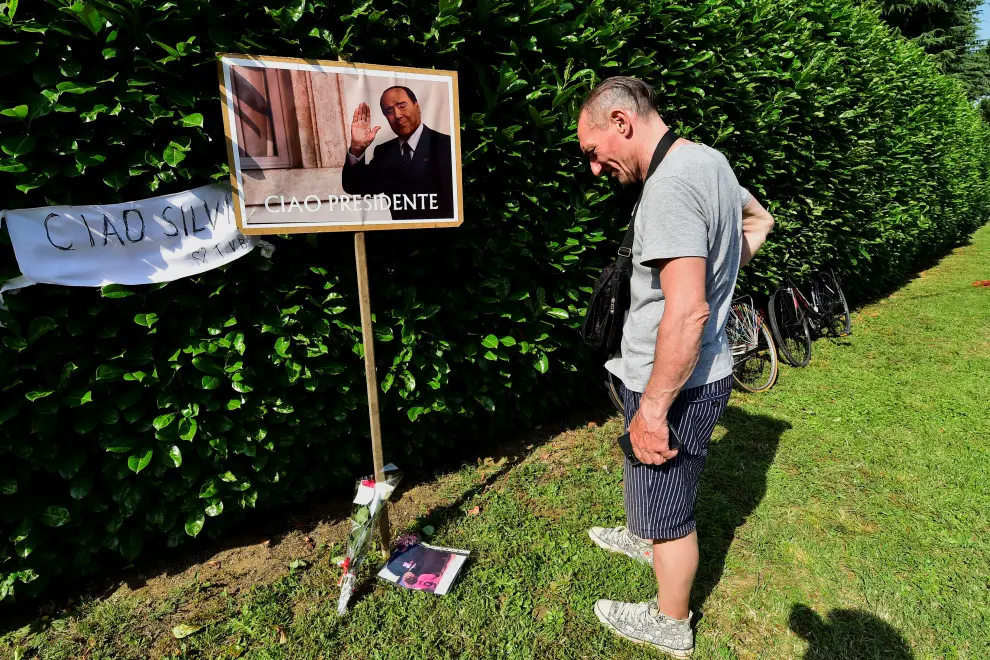 A person crouches next to flowers and football memoriabilia as people pay their respects outside former Italian Prime Minister Silvio Berlusconi's house, to which his body was transported following his death, in Arcore near Milan, Italy, June 12, 2023. REUTERS/Massimo Pinca  ITALY-BERLUSCONI/