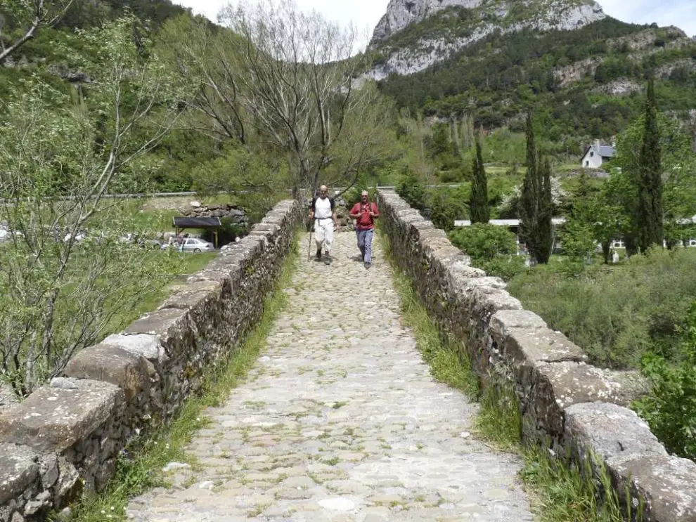 Dos peregrinos cruzan el puente de origen medieval (reconstruido en el XVI) de Canfranc pueblo
