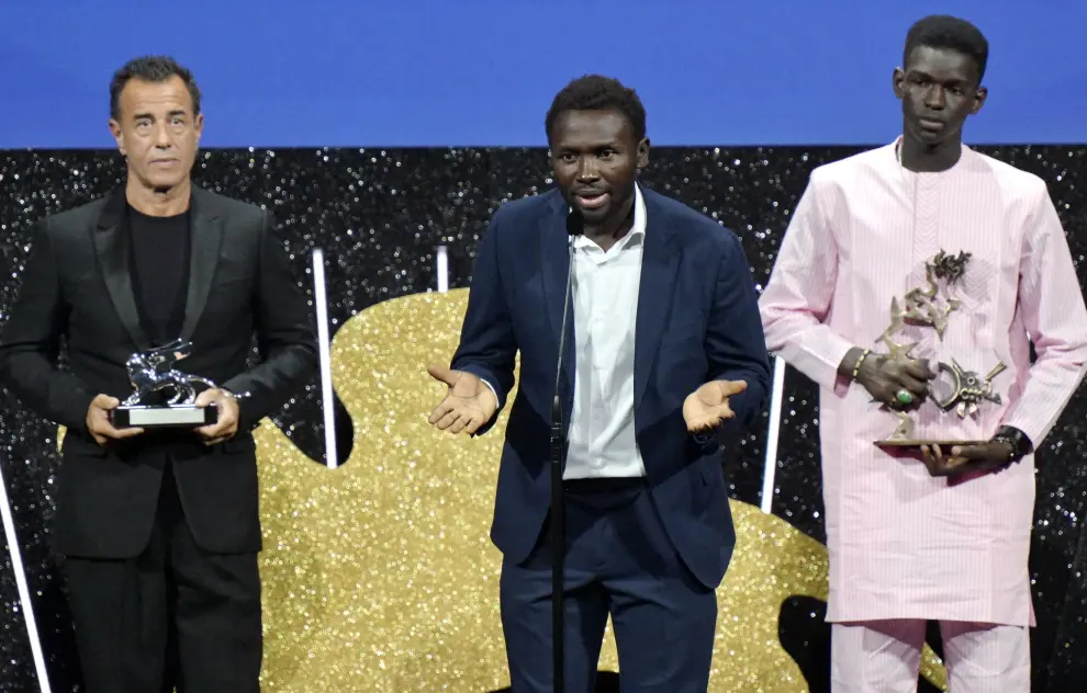 Venice (Italy), 09/09/2023.- Italian director Matteo Garrone (L) holds the Silver Lion for Best Director for 'Io Capitano (Me Captain)' and Senegalese actor Seydou (R) Sarr holds the 'Marcello Mastroianni' Award for Best New Young Actor for his performance in the movie as actor/cast member Mamadou Kouassi (C) speaks during the closing and awards ceremony of the 80th annual Venice International Film Festival, in Venice, Italy, 09 September 2023. The film festival runs from 30 August to 09 September 2023. (Cine, Cine, Italia, Niza, Venecia) EFE/EPA/ETTORE FERRARI

