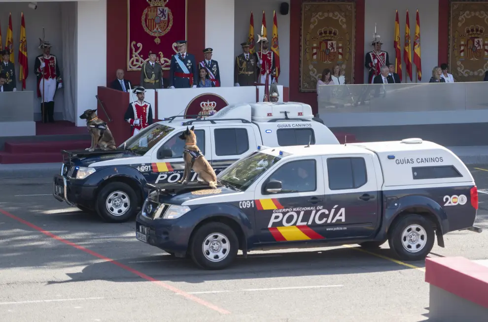 Vehículos de la Policía Nacional pasan por la tribuna real durante el desfile con dos perros sobre el capó.