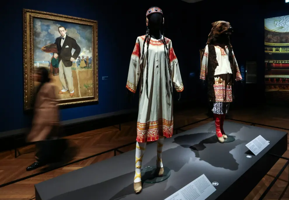 Una mujer pasa junto a las obras de arte 'Traje para la elegida' (centro), 'Traje para la joven de rojo' (derecha) de Nicolas Roerich e 'Igor Stravinsky' (izquierda) de Jacques-Elily Blanche