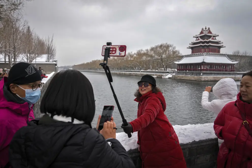 A woman takes a selfie with the Turret of the Forbidden City after a snow fall in Beijing, Monday, Dec. 11, 2023. An overnight snowfall across much of northern China prompted road closures and the suspension of classes and train service on Monday.(AP Photo/Andy Wong)