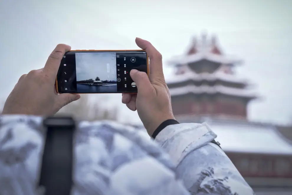 A resident takes a smartphone photo of the snow covered Turret of the Forbidden City in Beijing, Monday, Dec. 11, 2023. An overnight snowfall across much of northern China prompted road closures and the suspension of classes and train service on Monday.(AP Photo/Andy Wong)