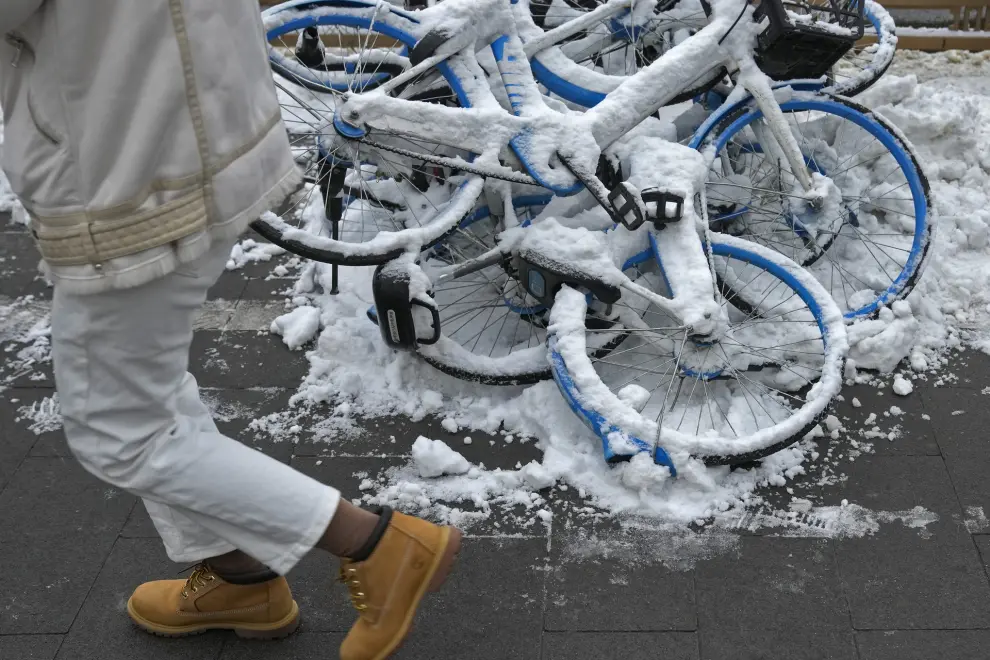 A resident walks by snow covered bicycle of bike-sharing companies piled up on a sidewalk after a snow fall in Beijing, Monday, Dec. 11, 2023. An overnight snowfall across much of northern China prompted road closures and the suspension of classes and train service on Monday. (AP Photo/Andy Wong)