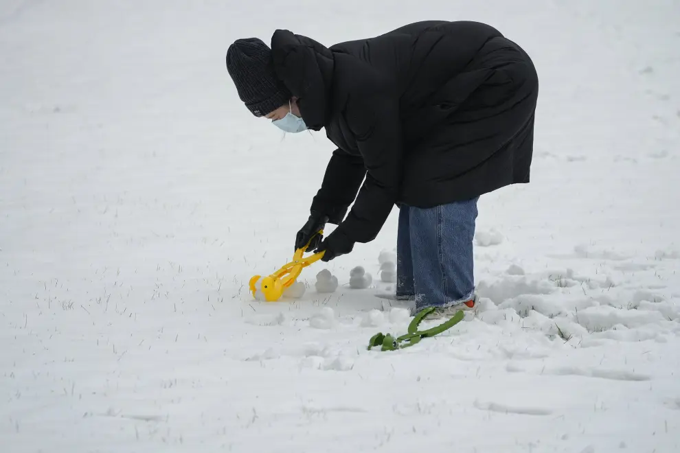 A woman makes snowballs in the shape of duck at an office building complex, after a snowfall in Beijing, Monday, Dec. 11, 2023. An overnight snowfall across much of northern China prompted road closures and the suspension of classes and train service on Monday. (AP Photo/Andy Wong)